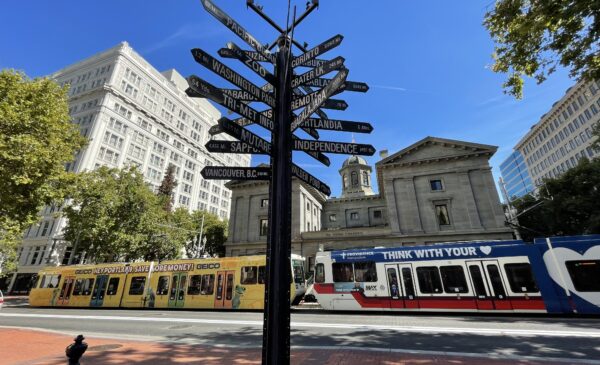Mile Post Sign in Pioneer Courthouse Square showing Portlands nine sister-cities and other worldwide destinations. A MAX train is going down the street behind it.