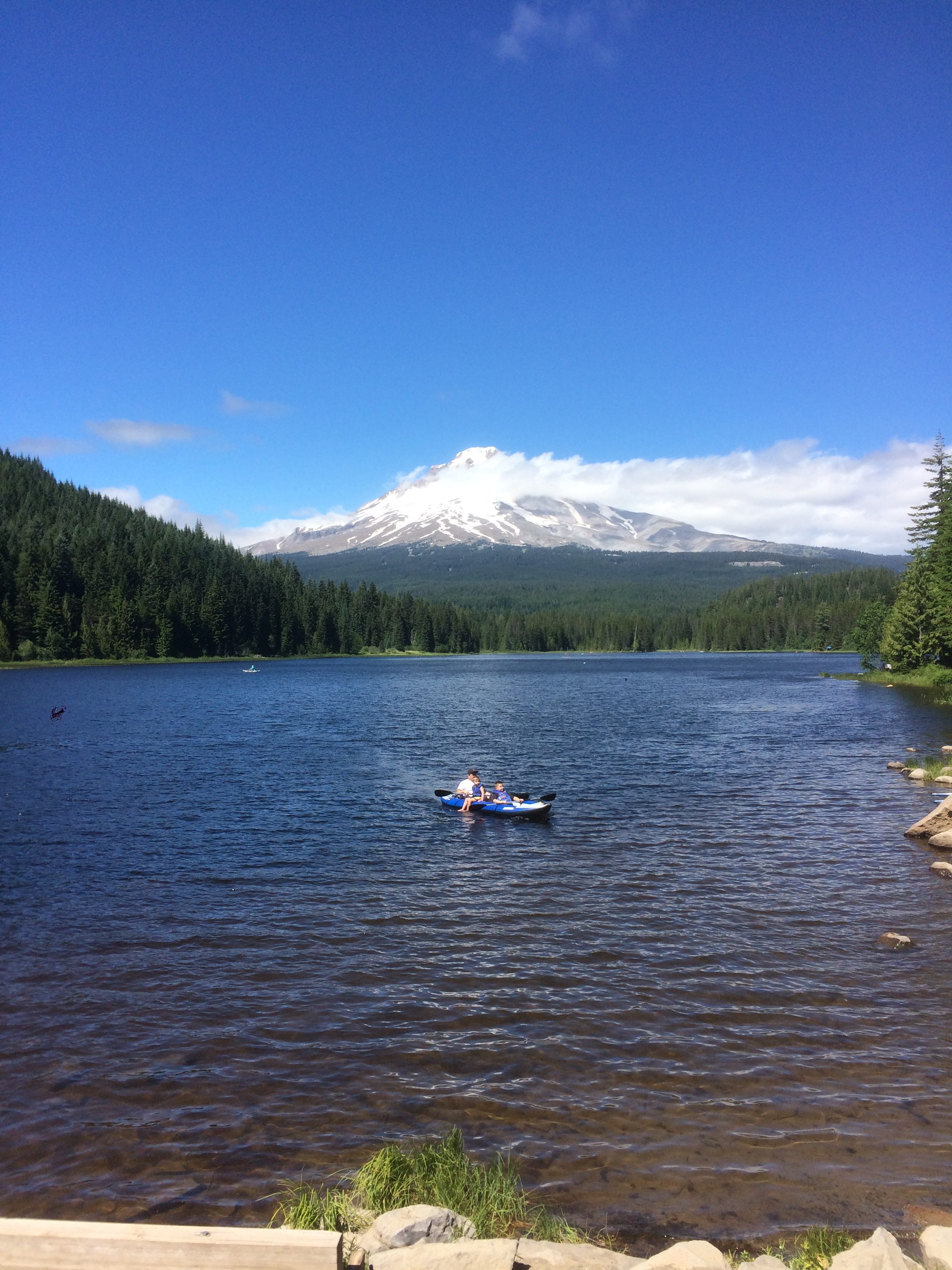 Mount Hood rising towards the sky above a blue mountain lake with a kayaker on it.