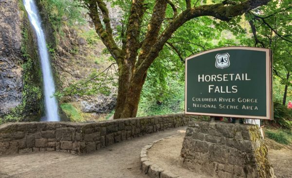 Horsetail Falls falling down the rocky side of a mountain. In front of that is a sign for the waterfall.